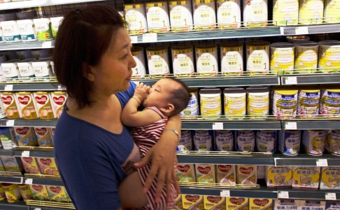 A woman carries a child passing through powdered milk products at a supermarket in Beijing. Photo: AP