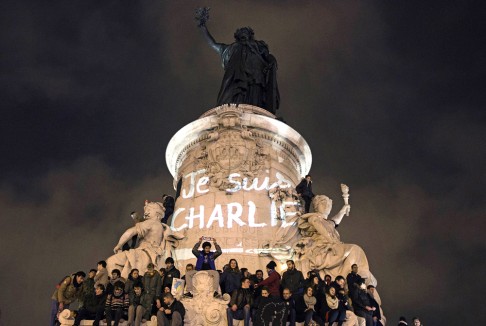 In a rally to show solidarity for the victims of the attack on the Charlie Hebdo offices, people stand on the statue of the Republic square next to a graffiti reading "I am Charlie" in Paris. Photo: AFP