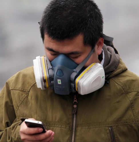 A man wearing a mask uses his mobile phone amid heavy smog after the city issued its first ever "red alert" for air pollution, in Beijing. Photo: Simon Song